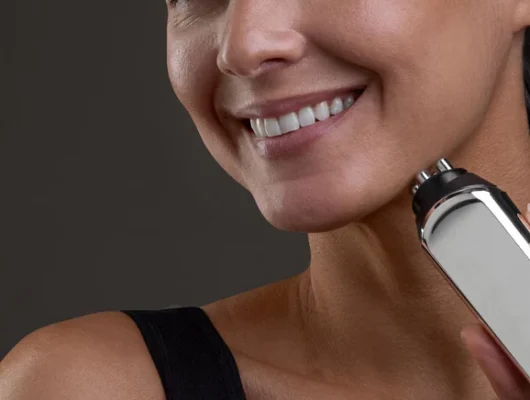 Mujer usando dispositivo de radiofrecuencia facial en casa para reafirmar la piel